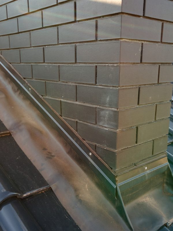 Closeup of brick chimney on house roof top covered with ceramic shingles. Tiled covering of building