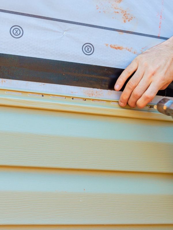 Hands working on house siding installation with hammer and protective materials during daytime Hands working on house siding installation with hammer and protective materials during daytime