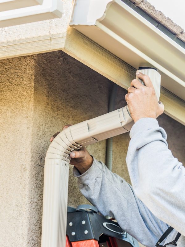 Worker Attaching Aluminum Rain Gutter and Down Spout to Fascia of House